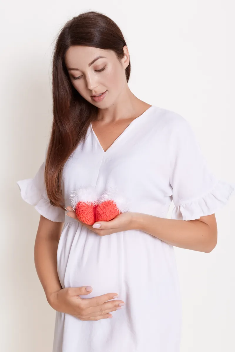beautiful pregnant woman with red baby shoes isolated