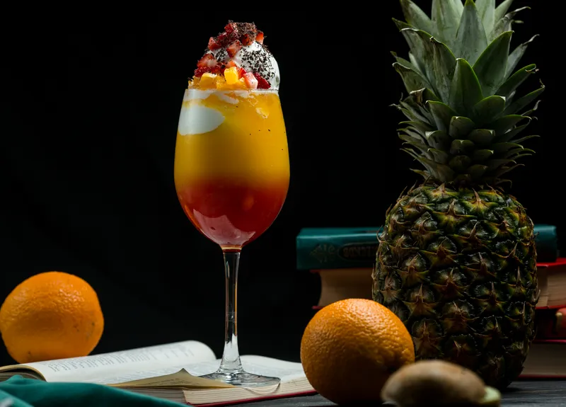 glass full mixed tropical fruits cocktail with rich colors standing book leaves
