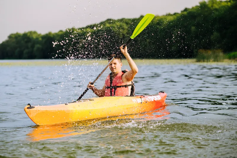 man splashing water with paddle while kayaking lake