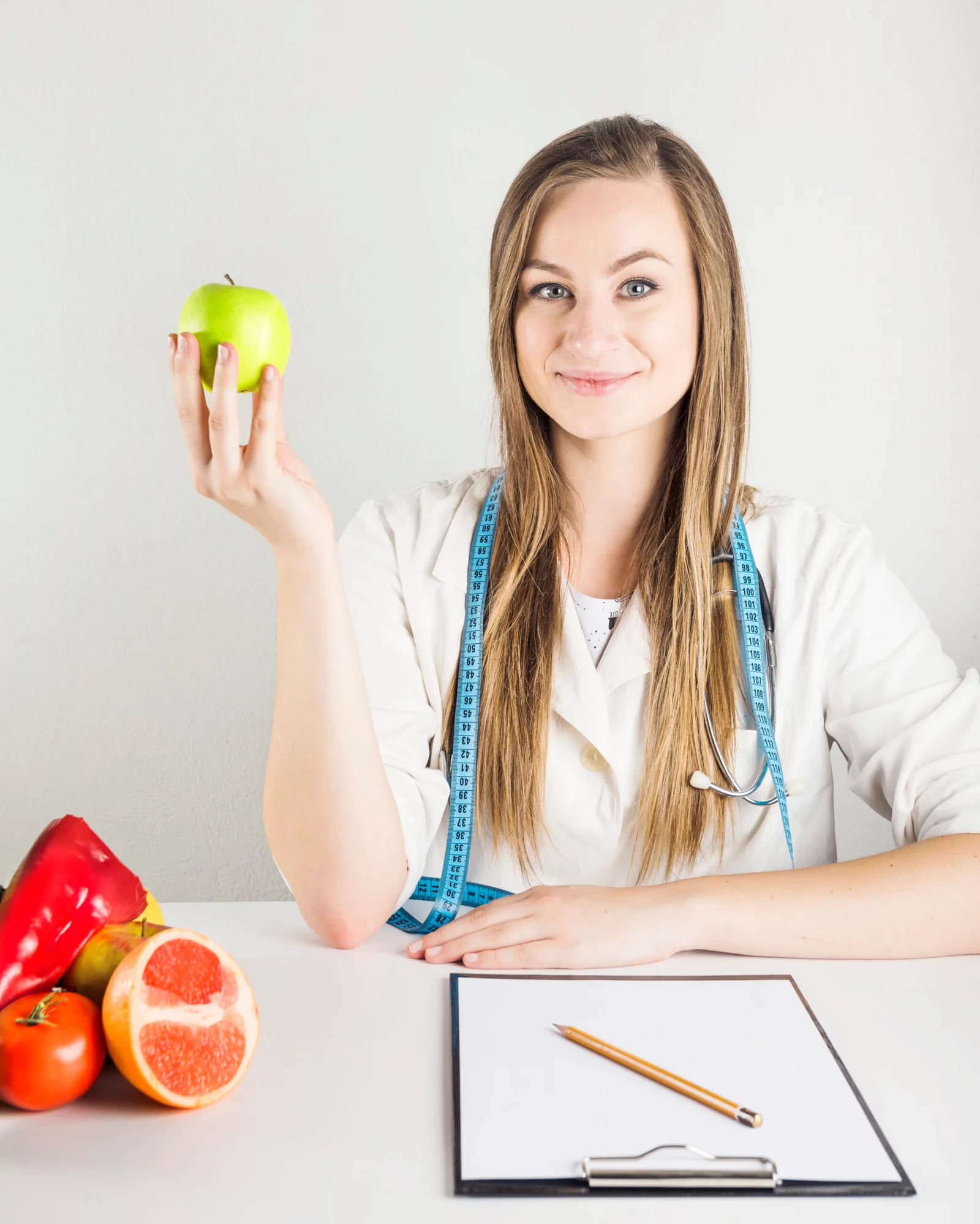 young-female-dietician-holding-green-apple-with-food-clipboard-desk